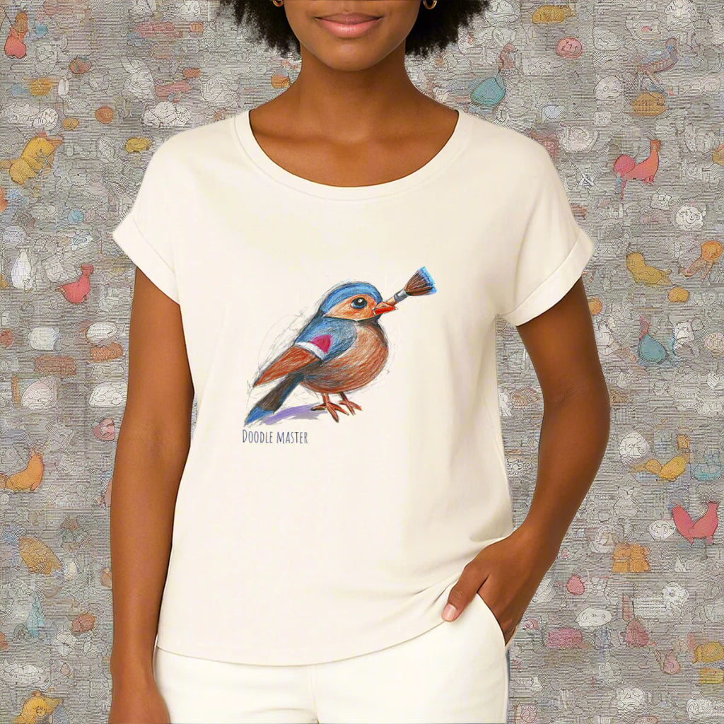 A woman wearing an ivory colored t-shirt with cuffed sleeves. On the fron is a pencil drawing of a little bird, holding a paint brush and the text doodle master. By Rosenmay Studio